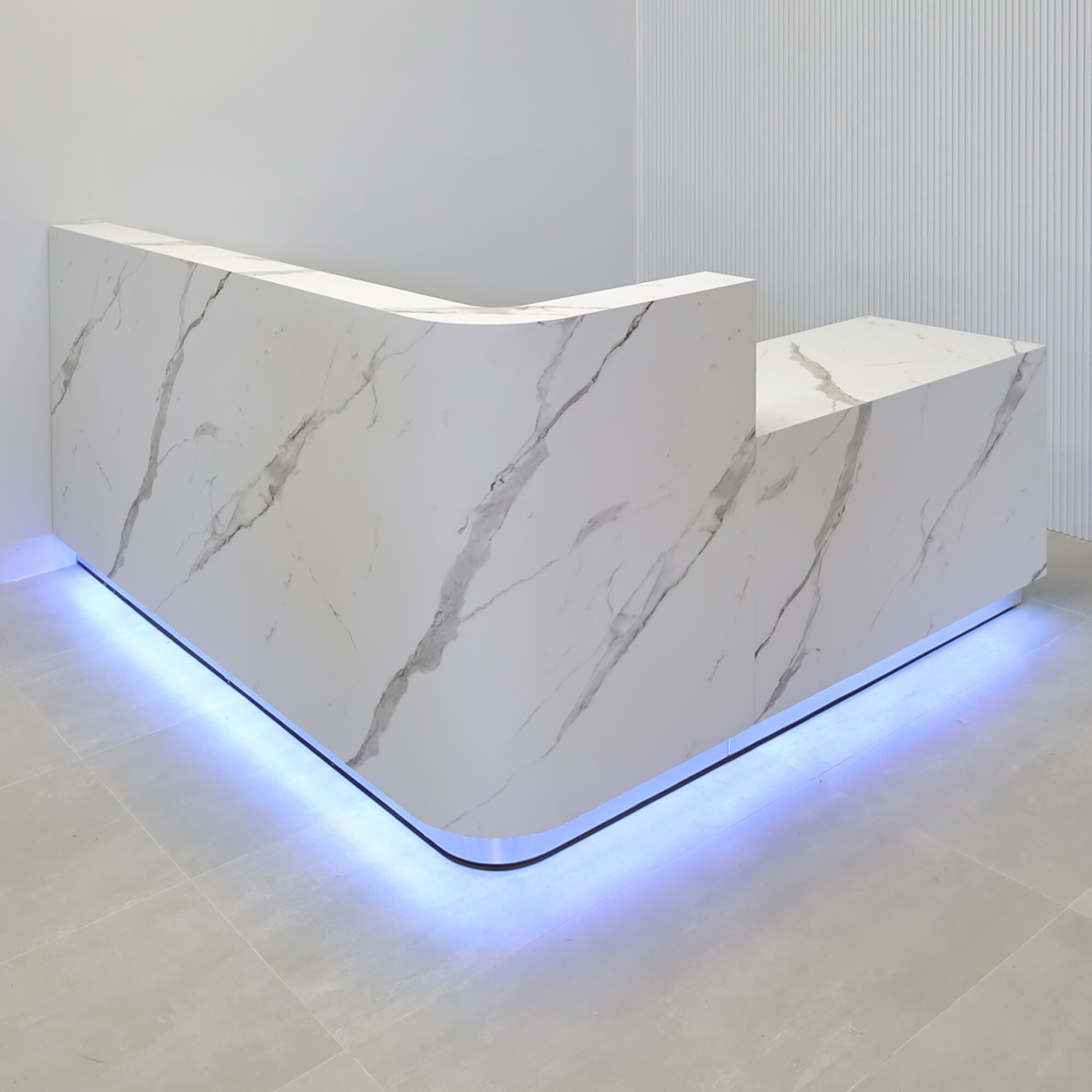 90-inch Nola L-Shape Custom Reception Desk with the l-panel on the right side when facing front with a 36-inch low extension. The main desk is covered in calcutta stone PVC, the toe-kick in brushed aluminum, and comes with color changing LED.