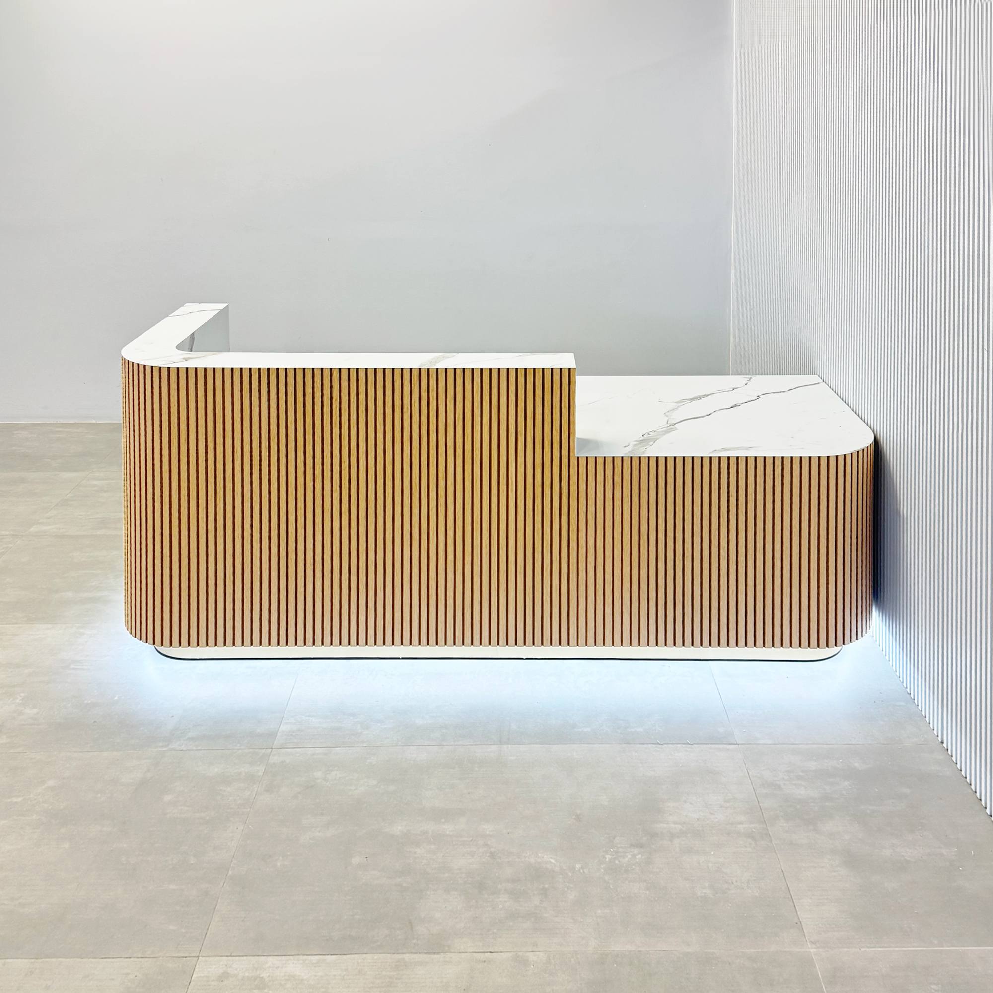 90-inch Nola Low Counter Reception Desk with white oak tambour desk, calcutta stone PVC laminate workspace & storage, gold aluminum toe-kick, and white LED.
